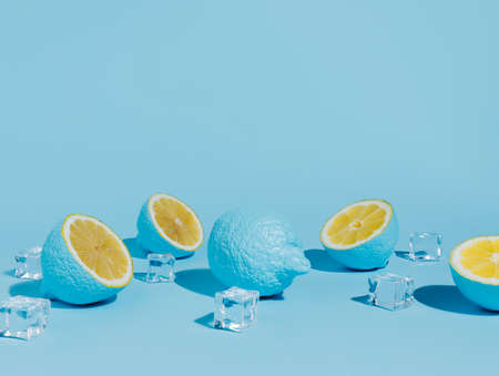 Blue painted lemon fruit with ice cubes on vibrant blue background. Creative summer food and drink concept. Tropical vegetarian fruit.の写真素材