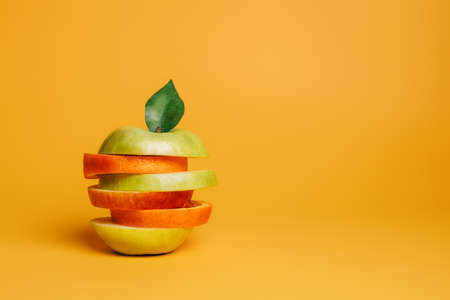 Orange and apple slices stacked vertically on the vibrant orange background. Creative fruit concept. Minimal food poster for vitamins, healthy diet or organic cosmetics.の写真素材