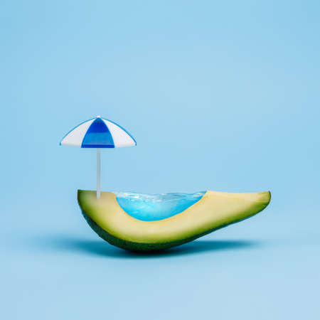 Swimming pool made of avocado fruit and sun umbrella. Creative minimal summer idea. Surreal vacation concept.の写真素材