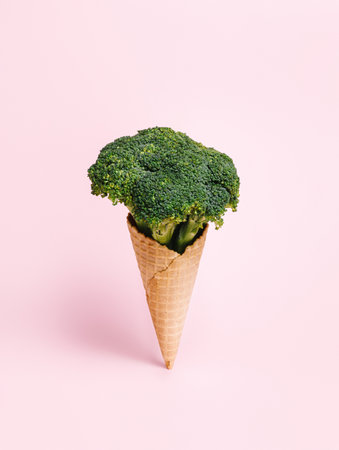 Fresh broccoli in an ice cream cone on pastel pink background. Waffle cone with a vegetable as a vegetarian dessert. Creative healthy food concept.の写真素材