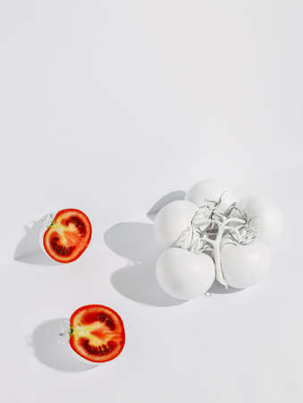 Branch of ripe tomatoes painted in white and two halves of cut red tomatoes isolated on a white...