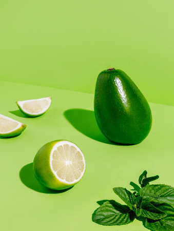 Slices of lime, mint leaves, and ripe avocado on a bright green background. Summer cocktail ingredients. Fresh and healthy food arrangement. Creative fruit concept.の写真素材