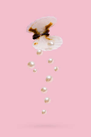 Glossy pearls dropped from a seashell isolated on a pastel pink background. Elegant, natural pearls...