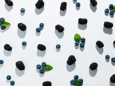 Assortment of blackberries and blueberries with green mint leaves isolated on a bright white background. Creative food concept. Minimal vegetarian healthy diet texture with summer shadows. Flat lay.の写真素材
