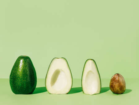 Whole fresh avocado fruit and two halves  in a row with a seed isolated on a mint green background....