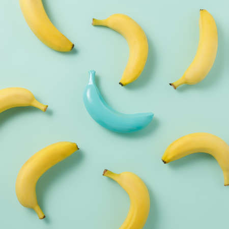Pattern with fresh yellow bananas and one banana painted in blue isolated on a light blue background. Difference or uniqueness texture. Creative fruit food concept. Flat lay, top view.の写真素材