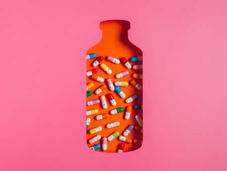 Orange bottle container as a remedy for illnesses with colorful pills isolated on a pink background. Medicine and drug inspired photography. Doctor's prescription. Creative pharmacy concept.の写真素材