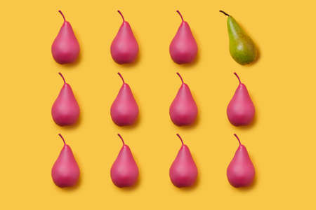 Pattern of pink painted pears on vibrant yellow background with one green pear. Differentiation and unique idea. Creative fruit food texture concept.の写真素材