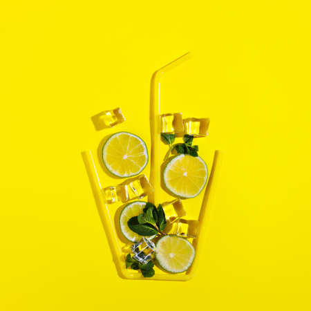 Glass shape made with straws with cut lemons, ice cubes, and mint leaves leaves inside isolated on a bright yellow background. Summer refreshing drink, cocktail ingredients. Creative drink concept.の写真素材