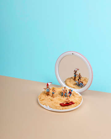Collapsible mirror with human miniature toys, sand and beach equipment inside. Creative summer vacation concept.の写真素材