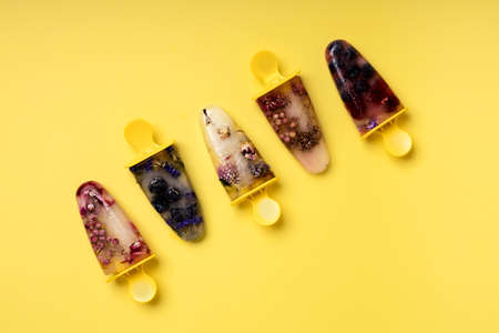 Five frozen ice cream  vertically arranged, isolated on vibrant yellow background. Fruity and transparent homemade ice creams made of berries and herbs. Creative summer sweet food concept.の写真素材