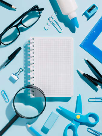 School or office stationery on blue background. Magnifier, glasses, notebook, ruler, pens, and other office equipment. Creative office or back to school concept with copy space. Flat lay, top view.の写真素材