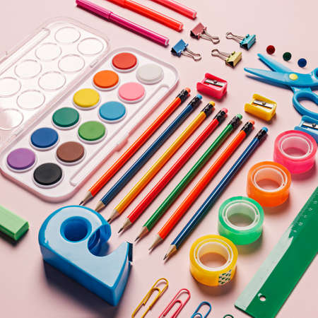 Set of student's school equipment isolated on a pastel pink background. Essential office set, colorful pencils, watercolors, clips, pins, and erasers. Creative school or office concept. Flat lay.の写真素材