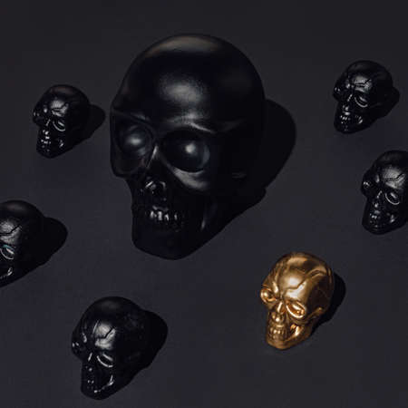 A pattern of tiny black and golden human skulls isolated on a black background. Creative Halloween or Day of the Dead concept. Minimal spooky cult aesthetic. Luxurious macabre texture.の写真素材