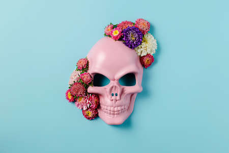 Pink plastic skull surrounded by floral arrangement isolated on a vibrant blue background. Creative Halloween or Day of the Dead concept. Magical surreal idea. Flat lay.の写真素材