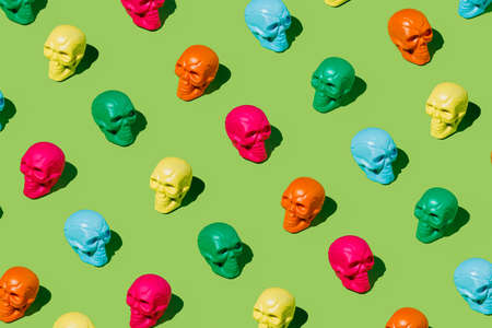 Creepy and spooky pattern of colorful human skulls isolated on a vivid neon green background. Creative Halloween or Day Of The Dead concept. Fashion retro future aesthetic. Flat lay.の写真素材