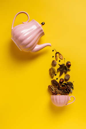 Creative layout with tea pot pouring autumn dry flowers, acorns and leaves into tea cup on vibrant yellow background. Creative fall season concept. Still life visual trend. Flat lay.の写真素材