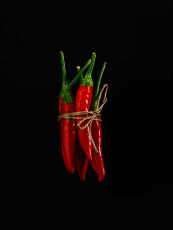 Red hot chili peppers bound with tiny rope levitate against black background. Creative spicy food concept. Minimal cooking ingredient idea.の写真素材