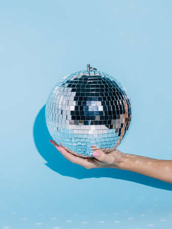 Shiny disco ball in a woman's hand isolated on a bright blue background. Ball part effect, nightlife, and celebration inspired idea. Creative New Year party or festive concept. Fashion minimal art.の写真素材
