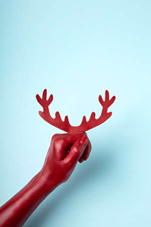 Woman's hand painted in red holding fake reindeer horns on pastel blue background. Santa Clause helper. Creative Christmas or New year celebration concept. Minimal visual trend.の写真素材