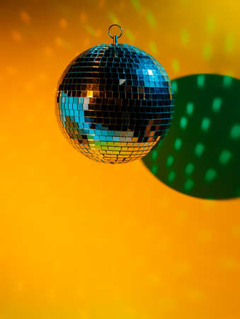 Party disco mirror ball reflecting colorful lights on a yellow wall. Nightlife and nightclub decoration. Dance and music-inspired backdrop. Creative party concept.の写真素材
