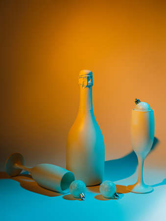 Neon composition with white champagne bottle, two glasses and Xmas ornaments. Creative  New Year and Christmas party concept. Festive holiday gradient holographic background. Iridescent visual trend.の写真素材