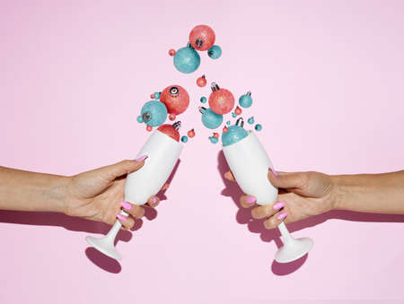 White champagne glasses toast with splashing out ornaments on a pastel pink background. Creative Christmas or New Year celebration party concept. Minimal December holiday idea. Visual trend backdrop.の写真素材