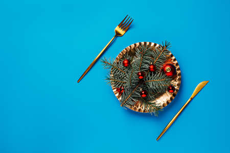 Christmas table setting with golden knife, fork and plate fir branches and red ornaments on vibrant blue background. Holiday preparation for Xmas dinner. Creative festive food concept. Flat lay.の写真素材