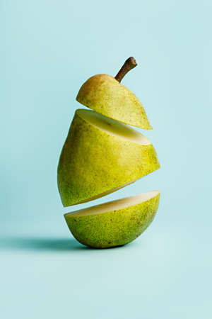 A juicy and ripe fresh pear cut into levitating slices isolated on pastel blue background. Sweet and healthy summer and autumn fruit. Minimal organic and vegan diet backdrop. Creative food concept.の写真素材