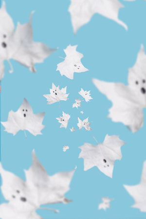 Ghost-looking white maple leaves flying in the air on a light blue pastel background. Creative Halloween party concept. Minimal scary holiday visual rend.の写真素材