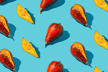 A pattern of whole autumn gourdes and cut into slices on a vivid blue background. Creative Halloween and Thanksgiving creative concept. Minimal food or fall harvest composition. Flat lay.の写真素材