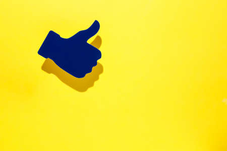 Blue thumb up icon on vibrant yellow background. Creative success or social network concept. Minimal backdrop with copy space for text. Flat lay, top view.の写真素材