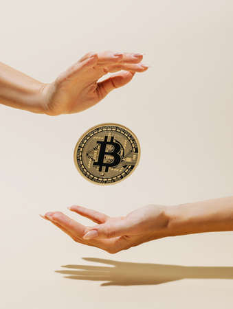 Golden bitcoin flying in the air and levitating between woman's hands on pastel beige background. Creative cryptocurrency or blockchain concept. Stock Market, digital gold money and stock business.の写真素材