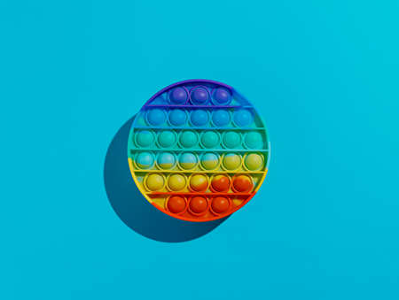 Pop it fidget toy with pokable bubbles in shape of colorful circle on vibrant blue background. Creative anti-stress toy concept. Trendy sensory anti anxiety sensory game. Flat lay, top view.の写真素材