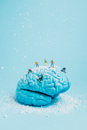 Miniature snowboarders on blue painted human brain with snow on pastel blue background. Creative winter sports concept. Extreme sports state of mind. Adrenaline rush.の写真素材