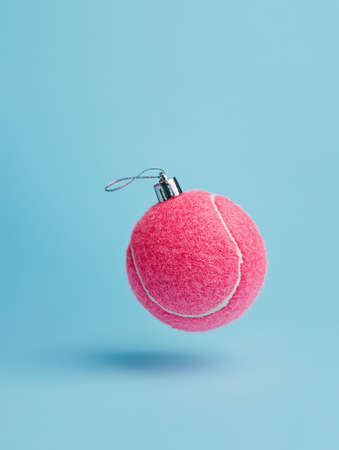 Creative Christmas layout made with flying pink tennis ball as a tree ornament vibrant red on pastel blue background. Minimal Xmas or New Year celebration concept. Minimal winter holidays idea.の写真素材