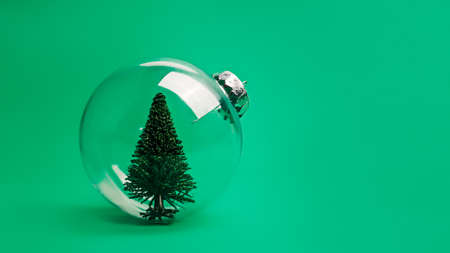 Creative Christmas composition with transparent glass ornament with pine tree inside on vivid green background. Minimal Xmas or New Year celebration concept. Minimal winter holidays idea. Copy space.の写真素材