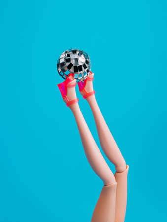 Creative Christmas party composition with doll leg in high heels and shiny disco ball on blue...