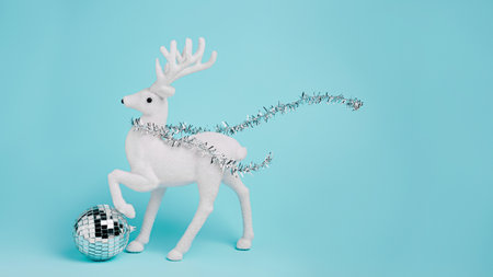 White reindeer with shiny disco ball and shawl isolated on pastel blue background. Creative Christmas and New Year celebration concept. Minimal festive banner with copy space. Seasonal greeting card.の写真素材