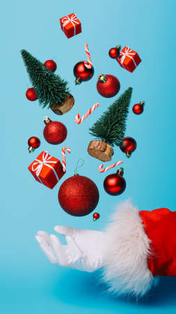 Creative Christmas composition with Santa Claus hand and flying bauble, pine tree and gift boxes on...