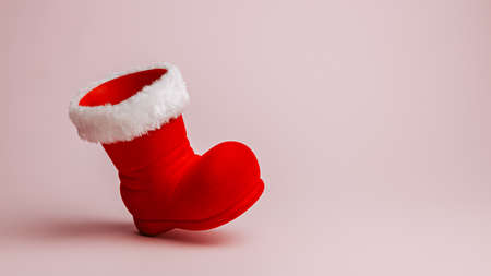 Santa Claus red boot on pastel pink background. Minimal Christmas eve or New Year celebration concept. Elegant winter holidays banner with copy space for text. Advertising or December sale shopping.の写真素材