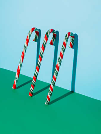 Red and Green Christmas candy canes leaning on the bright blue wall. Festive candies and sweet food. Creative Xmas and New Year creative concept. December winter holidays idea.の写真素材