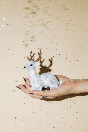 Christmas and New Year holidays concept. Female hand holding silver reindeer on beige background.の写真素材