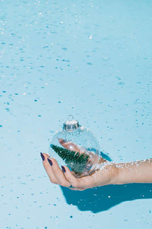 Woman's hand holds a glass Christmas ball on a blue background.