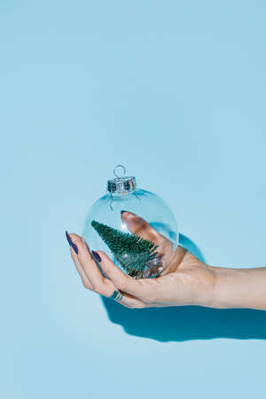 Female hand holds a glass Christmas ball on a blue background. Christmas and New Year concept.の写真素材