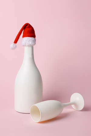 White bottle of champagne with Santa Claus hat on pink background. Christmas and New Year concept.の写真素材