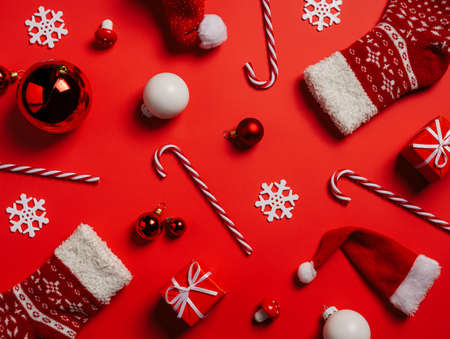 Festive Christmas pattern with candy canes, decorative balls, Santa's hats, gift boxes, and socks on red background. Creative Xmas celebration or New Year eve concept. Winter holiday idea. Flat lay.の写真素材
