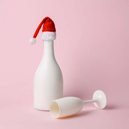 White champagne bottle with Santa Claus hat and wine glass on pastel background. New Year or Christmas midnight toast. Winter holiday season celebration concept. Minimal elegant drink idea.の写真素材