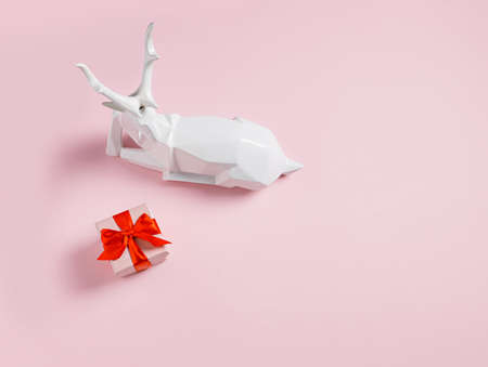 Christmas composition with white reindeer and red gift box on pastel pink background. Creative Xmas or New year concept. Minimal December celebration banner with copy space.の写真素材