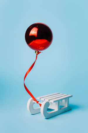 Red balloon and wooden sled on blue background. Minimal holiday concept.
